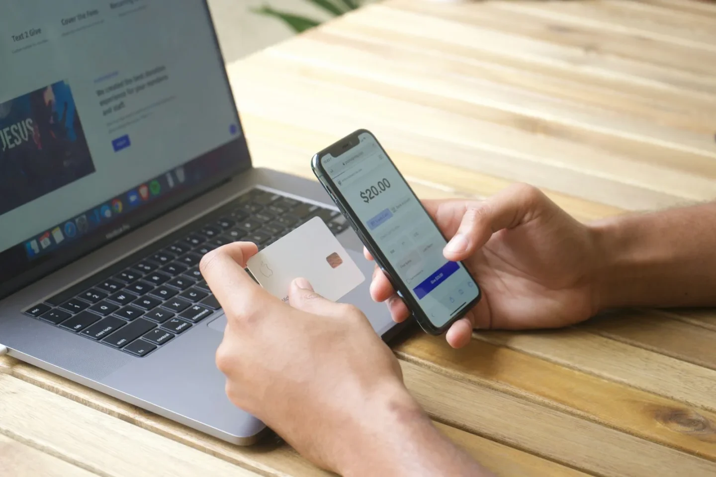 Händer som håller ett betalkort och en mobil med en betalning på skärmen, framför en öppen laptop