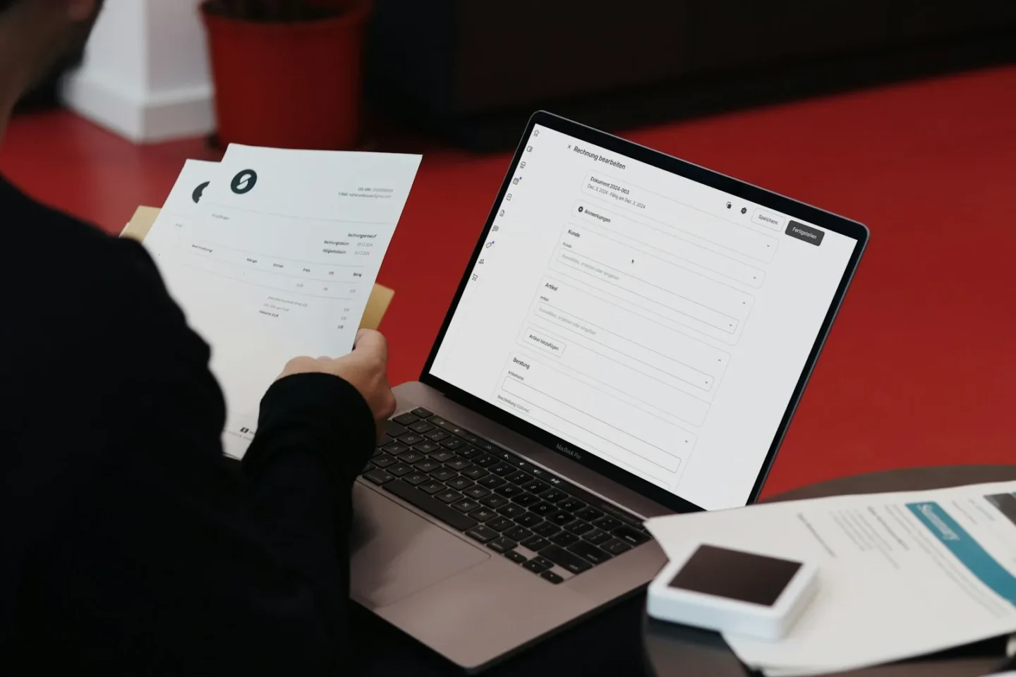Person som håller utskrivna fakturor framför en laptop där en faktura registreras i ett bokföringsprogram
