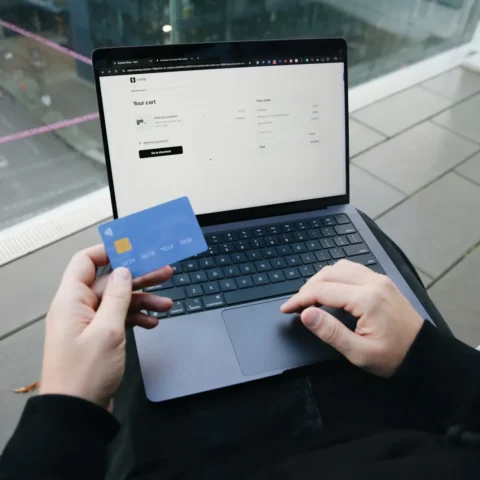Händer vid en laptop som visar varukorgen i en webbutik, med ett betalkort i handen